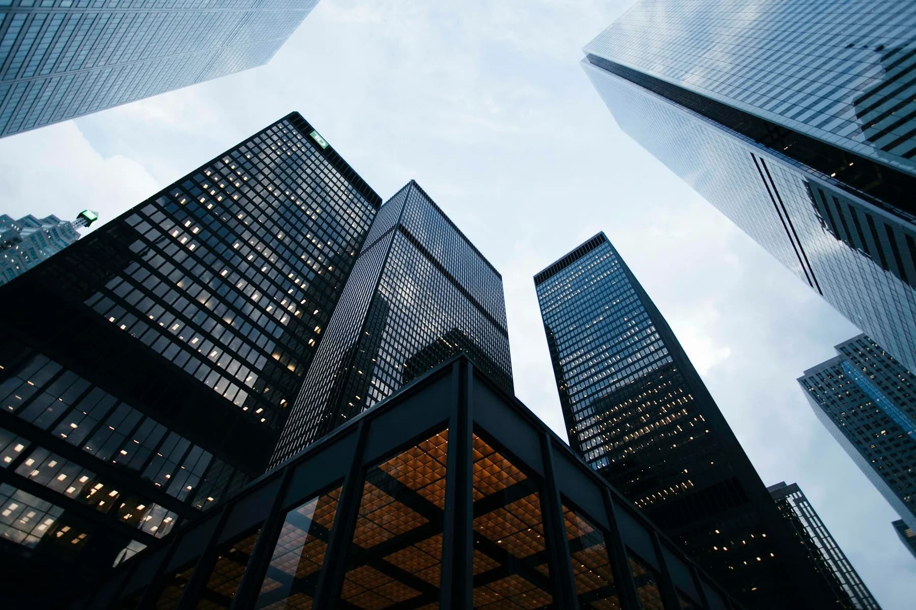 Glass office towers seen from street level, converging toward an overcast sky