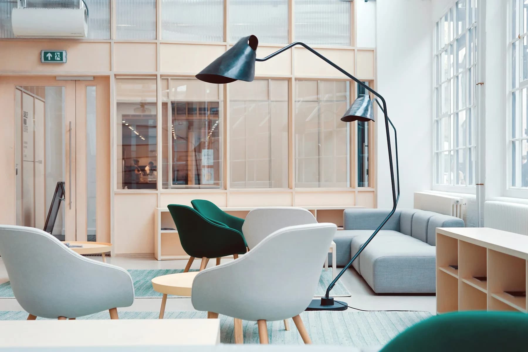 A quiet studio lounge with pale chairs, a floor lamp and glass partitions